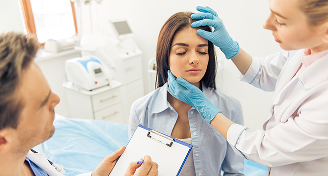 M�dico y enfermera revisando la cabeza y cuello de paciente.